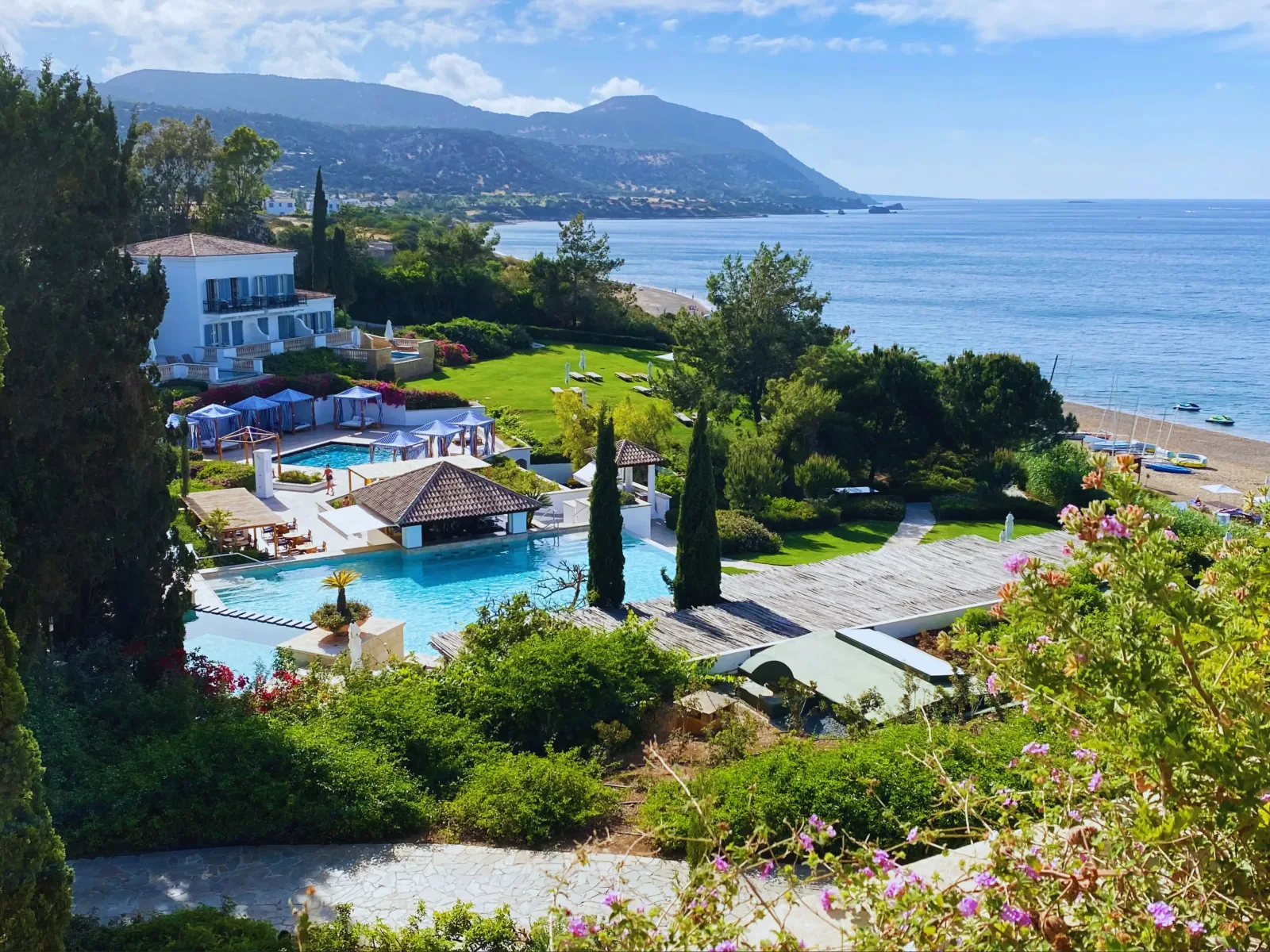 Scenic overlook of a luxury seaside resort with multiple swimming pools, lush gardens, and a clear view of the calm blue sea.