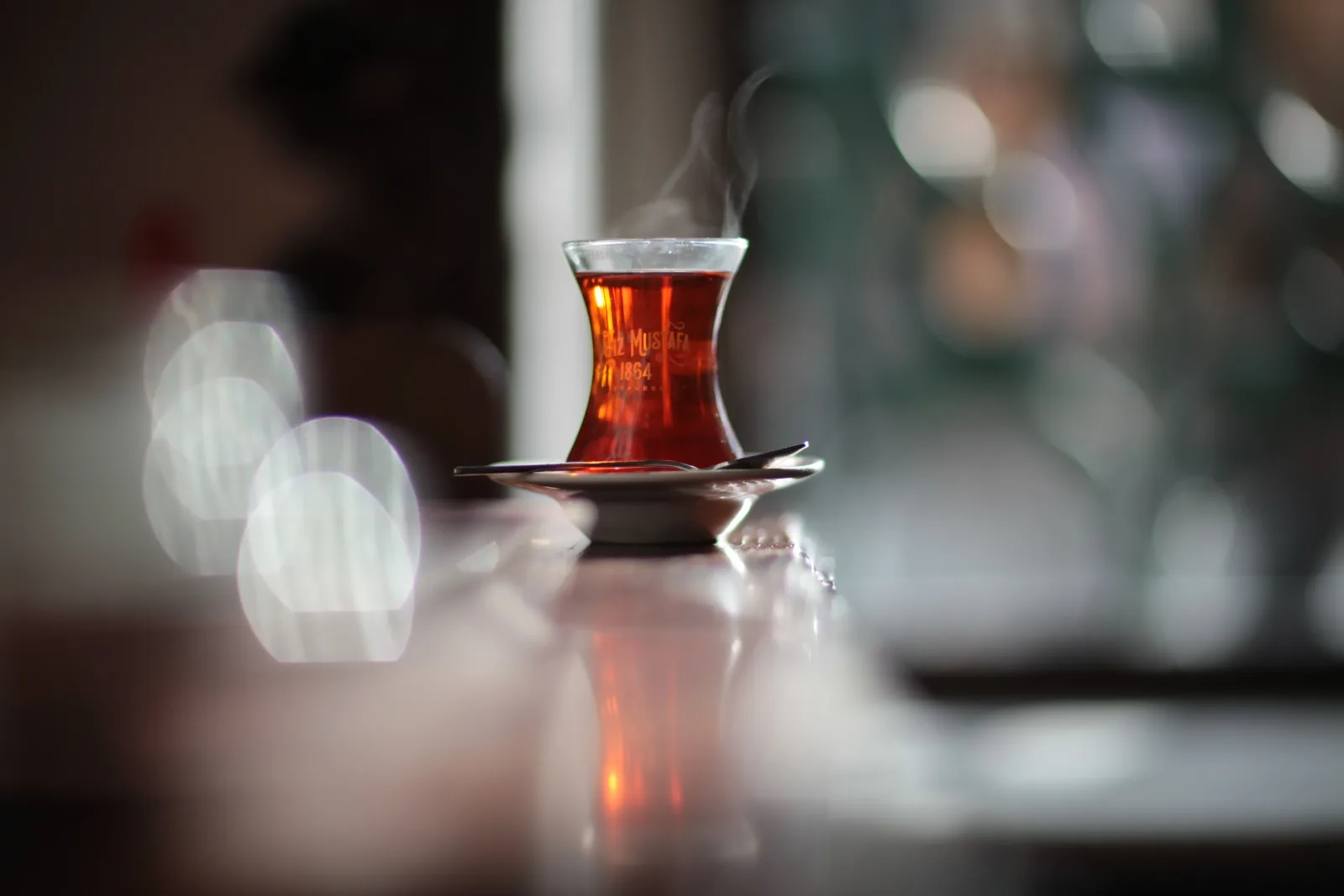Close-up of a traditional glass of tea, illuminated by sunlight, casting a warm glow and a soft reflection on a wooden surface.